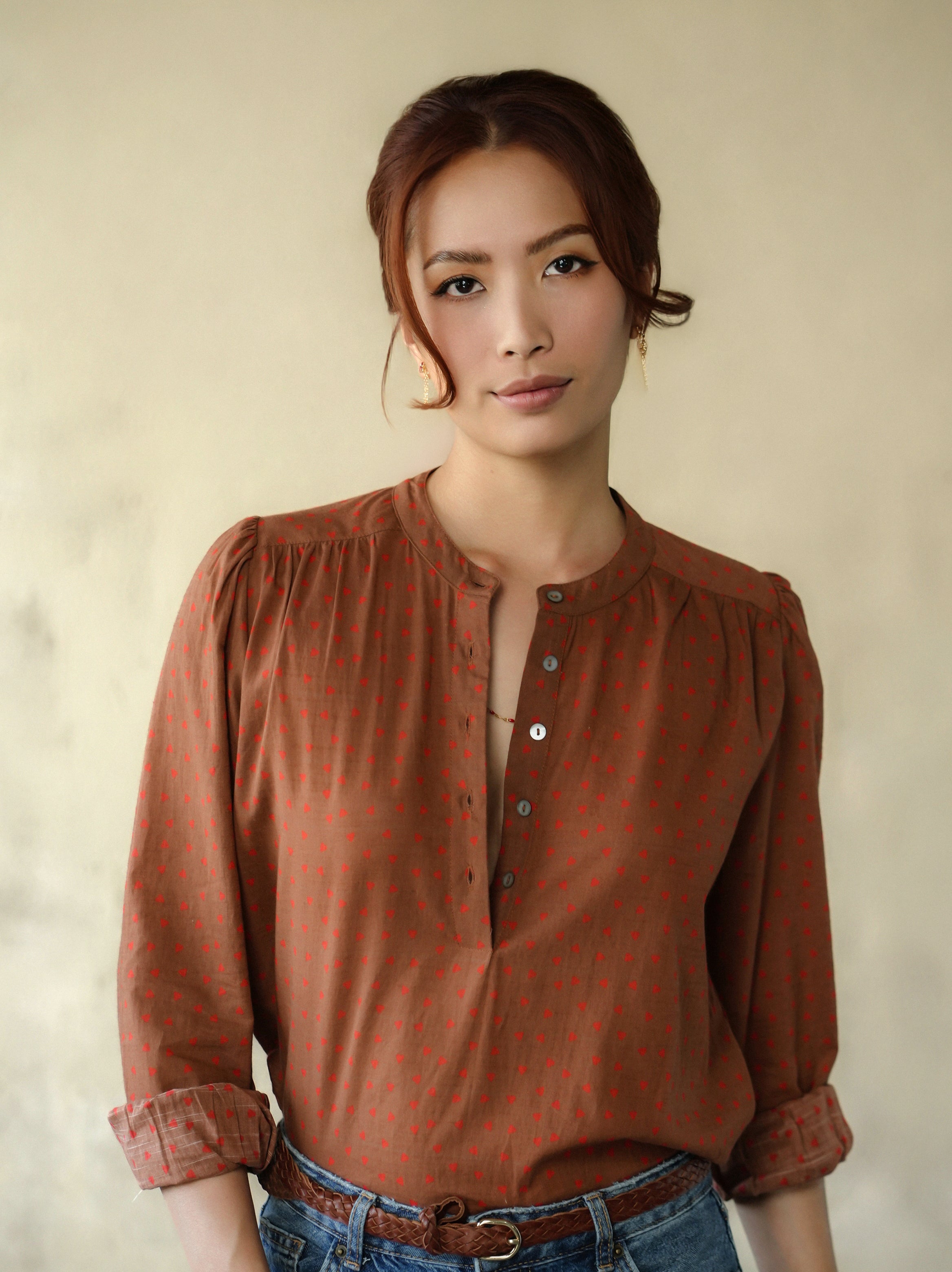 Woman wearing a brown patterned blouse against a beige background