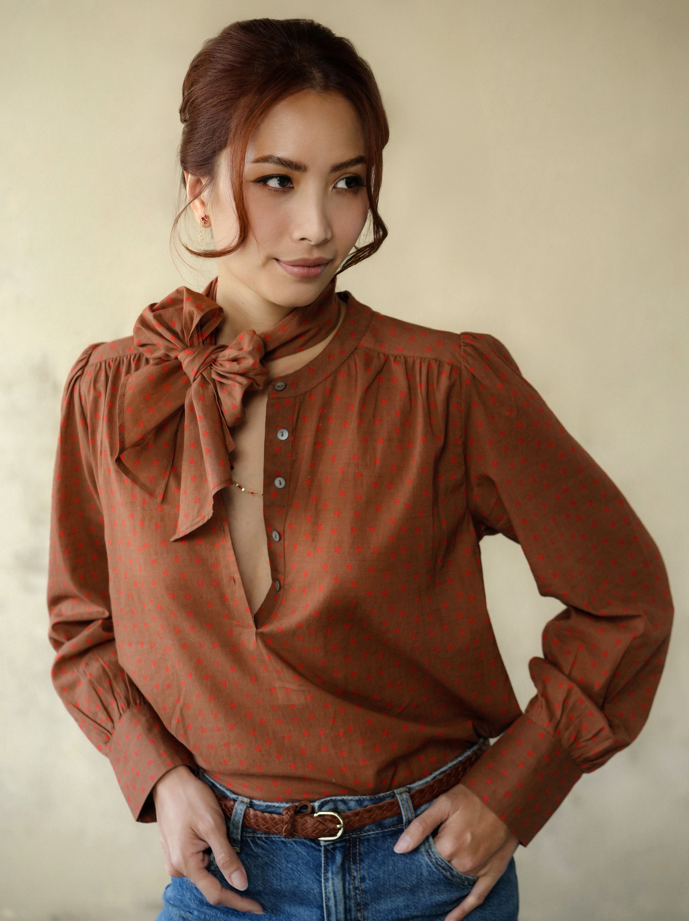 Woman wearing a brown blouse with a bow tie and blue jeans against a beige background