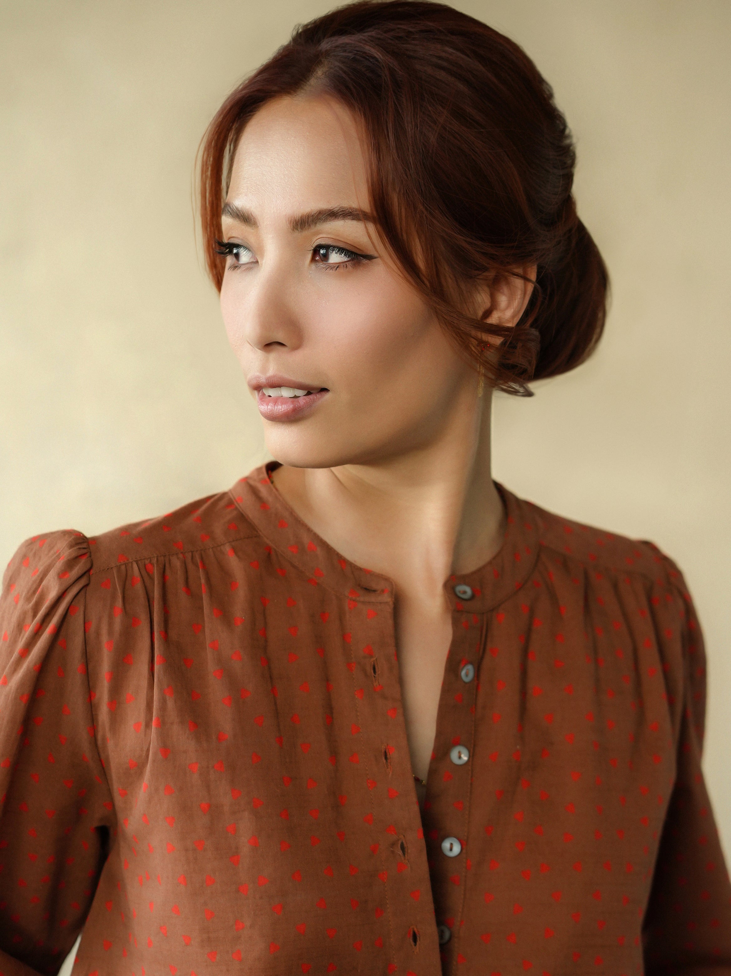 Woman wearing a brown blouse with red patterns against a beige background
