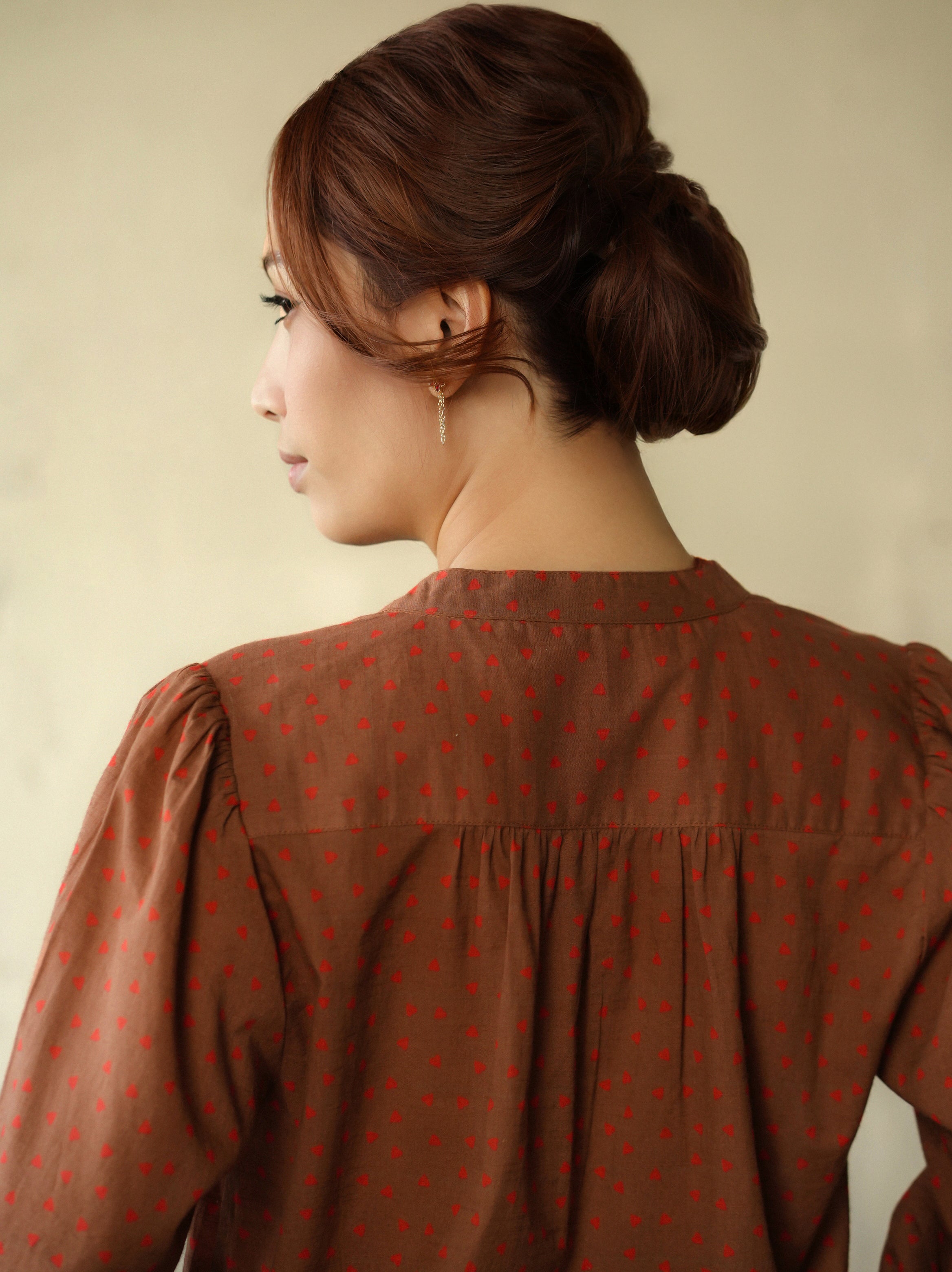 Woman wearing a brown blouse with red patterns against a beige background